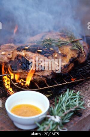 Jambe d'agneau, au caramel pour aplatir en étant barbecue au charbon de bois avec des noix de romarin et de pin, et 'brosse' faite de branches de romarin utilisées pour badir t Banque D'Images