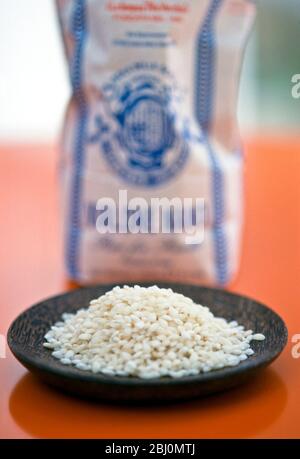 Riz italien arborio pour la fabrication de risotto, sur un petit plat en bois brun avec emballage en arrière-plan - Banque D'Images