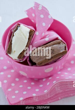 Rame de glace au chocolat et à la vanille dans des biscuits au chocolat maison enveloppés de serviettes en papier blanc et rose poteux, dans un bol assorti - Banque D'Images