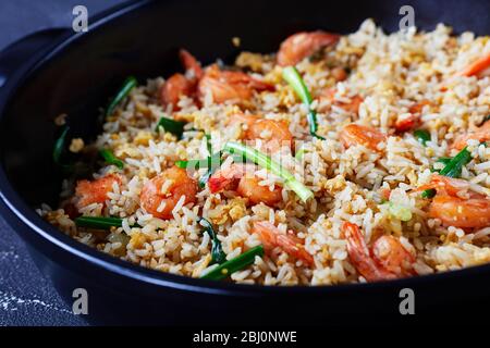 Riz au jasmin frit avec crevettes et oignons de printemps avec sauce thaï servi sur un plat noir sur fond de béton foncé, gros plan Banque D'Images