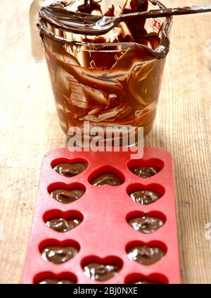 Créer un coeur en forme de chocolats pour la Saint-Valentin dans un moule rouge en forme de coeur, avec une carafe de chocolat messe - Banque D'Images