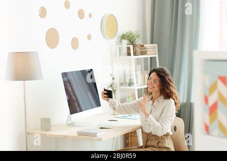 Une jeune femme élégante salue sa meilleure amie tout en ayant un appel vidéo sur son smartphone, prise de vue horizontale Banque D'Images