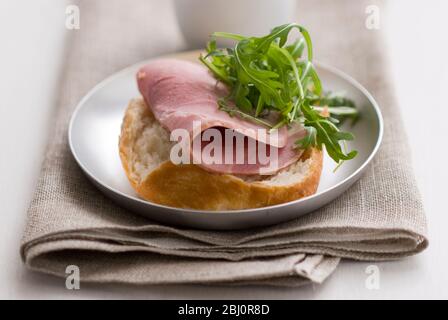 Sandwich ouvert de pain croustillant rouleau rustique, avec une tranche épaisse de jambon de qualité et une garniture de feuille de salade de roquette, avec une petite casserole de moutarde de Dijon - Banque D'Images