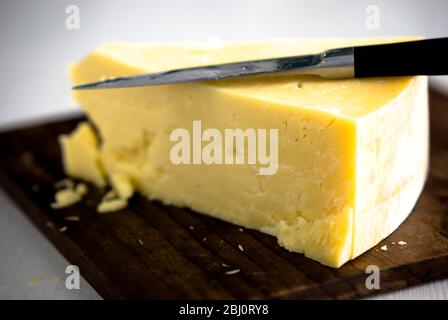 Cale de fromage cheddar, coupée sur un cheesboard en bois - Banque D'Images