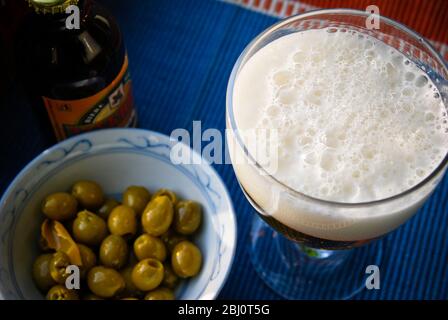 Verre de bière avec une bonne tête moussant, et un bol d'olives - Banque D'Images