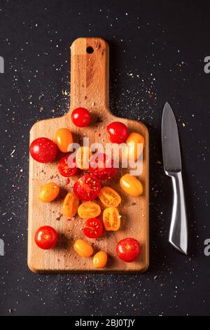 Différents cultivars de tomates sur un panneau en bois sur fond noir. Tomates multicolores Banque D'Images