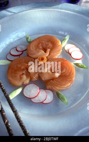 Sushis au saumon magnifiquement disposés sur une plaque de verre blanc givrée, dans un cadre formel à la table lors de la fête du déjeuner d'été en plein air, avec wasabi et radis blanc râpé Banque D'Images