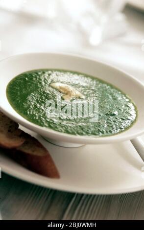 Soupe de pois verts frais délicats servie dans un bol blanc en chine sur plaque avec du pain français tasted - Banque D'Images