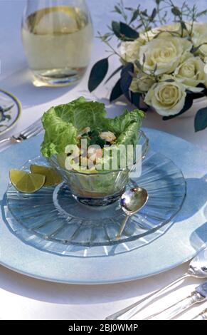 Salade de homard servie dans des feuilles de laitue dans un bol en verre cristal dans un cadre formel de table lors de la fête d'été en plein air, avec des roses et du vin blanc - Banque D'Images