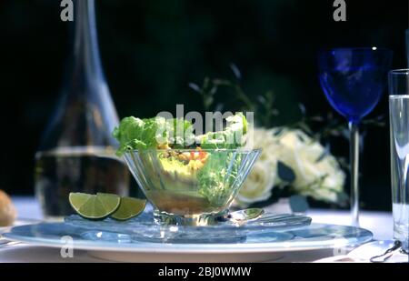 Salade de homard servie dans des feuilles de laitue dans un bol en verre cristal dans un cadre formel de table lors de la fête d'été en plein air, avec des roses et du vin blanc - Banque D'Images