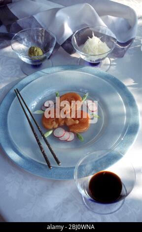 Sushis au saumon magnifiquement disposés sur une plaque de verre blanc givrée, dans un cadre formel à la table lors de la fête du déjeuner d'été en plein air, avec wasabi et radis blanc râpé Banque D'Images