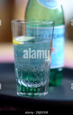 Verre de Pellegrino légèrement pétillant, eau minérale italienne, petit coin de citron sur plateau sombre - Banque D'Images