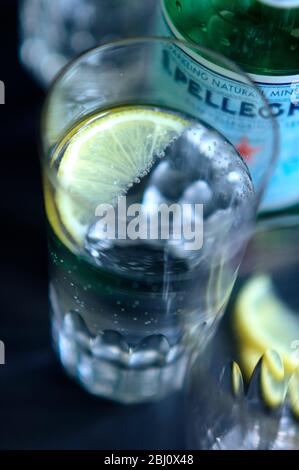 Verre de Pellegrino légèrement pétillant, eau minérale italienne, petit coin de citron sur plateau sombre - Banque D'Images