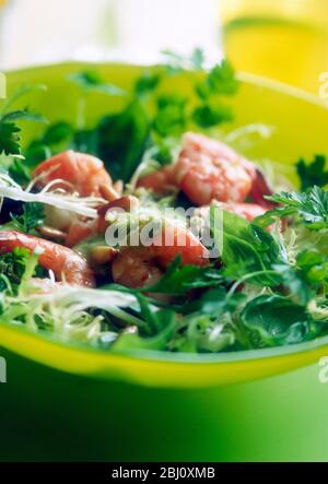 Crevettes géantes fraîches avec vinaigrette aux avocat et aux pignons sur salade de laitue frisée, feuilles de bébé, basilic, persil plat, dans un bol en verre vert - Banque D'Images