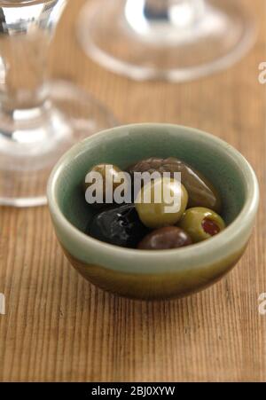 Olives italiennes dans un petit bol de poterie sur une surface rustique en bois avec des bases de verres à vin - Banque D'Images