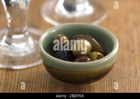 Olives italiennes dans un petit bol de poterie sur une surface rustique en bois avec des bases de verres à vin - Banque D'Images