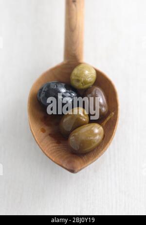 Cuillère en bois rustique avec olives italiennes mélangées, sur surface en bois peinte en blanc - Banque D'Images