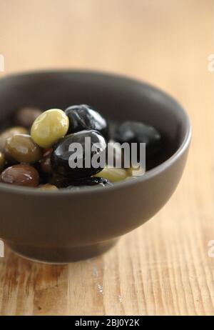 Olives italiennes mélangées dans un petit bol de poterie sur une surface en bois rustique - Banque D'Images