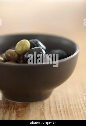 Olives italiennes mélangées dans un petit bol de poterie sur une surface en bois rustique - Banque D'Images