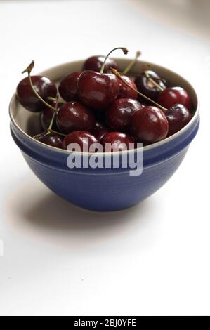 Un petit bol en céramique bleue de cerises rouges sucrées sur la surface blanche - Banque D'Images