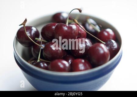 Un petit bol en céramique bleue de cerises rouges sucrées sur la surface blanche - Banque D'Images