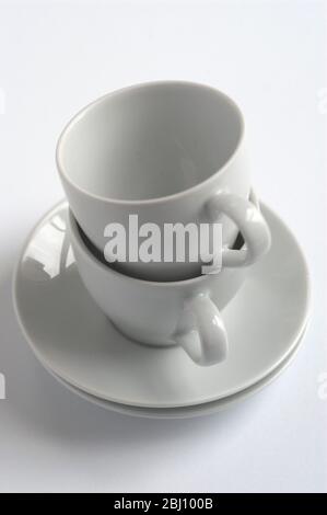 Deux tasses à café et soucoupes blanches empilées sur une surface blanche - Banque D'Images