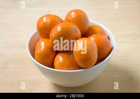 Satsumas dans un bol blanc sur table en bois - Banque D'Images