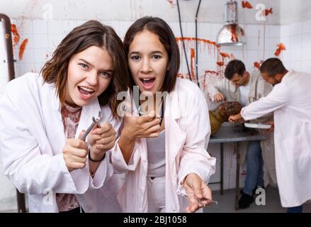 Deux jeunes filles s'amusant avec des amis masculins en quête prix en chambre chirurgicale avec des traces de sang, qui posent avec des instruments médicaux Banque D'Images