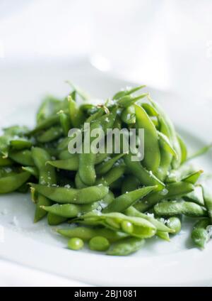 Haricots edamame cuits, sur une plaque blanche avec flocons de sel saupoudrés - en-cas à la mode adoptés du Japon - Banque D'Images