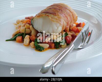 Filet de poisson-monkfish rôti enveloppé dans du bacon sur un lit de casserole de haricots - Banque D'Images