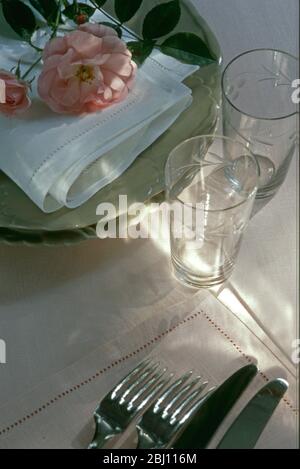 Préparez-vous à poser une table pour un dîner, en choisissant des verres couverts assiettes et serviettes avec une rose fraîchement cueilliée - Banque D'Images