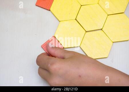 Puzzle géométrique enfant coloré à motif feuilles de tangram jaune et orange avec motif mains enfants et pièces mobiles vue du dessus. Banque D'Images