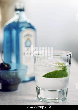 Verre de gin et tonique avec segment de chaux et bouteille de Bombay Sapphire en arrière-plan - Banque D'Images