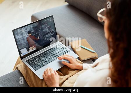 Femme imreconnaissable assise sur un canapé à la maison regardant la vidéo de conférence en ligne, prise de vue horizontale en grand angle Banque D'Images