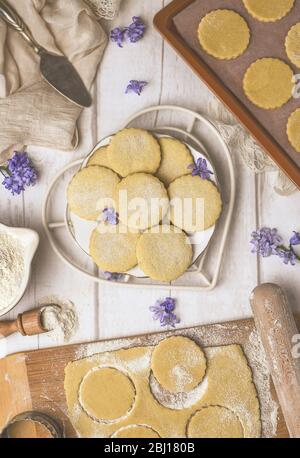 Vue de dessus de la plaque avec des biscuits aromatiques fraîchement cuits sur une table en bois blanc avec pâte brute et des fraises dans la farine Banque D'Images