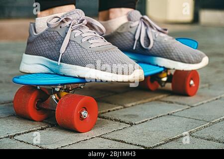 Photo des jambes d'une fille portant de vieilles baskets qui se tient sur un skateboard bleu sur un pavé, une mise au point sélective et un virage vintage. Tir de niveau Grownd. Banque D'Images