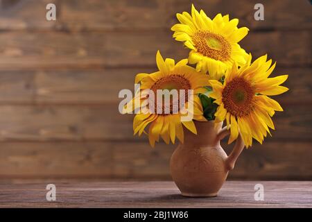 Belles fleurs de soleil vives dans le pichet sur fond en bois Banque D'Images