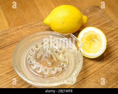 Jus de citron à partir d'un demi-citron pressé dans un presse-citron en verre avec un citron entier sur une planche à découper en bois Banque D'Images