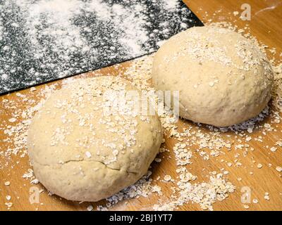 Deux ronds de pâte à pain d'avoine roulée dans l'avoine avec une plaque de cuisson farinée sur une table de cuisine Banque D'Images