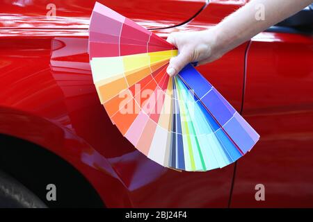 Main féminine avec échantillons de couleur sur fond rouge de voiture Banque D'Images