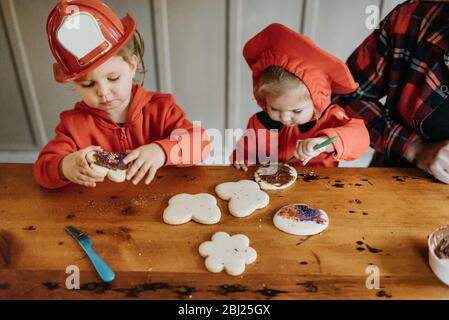 Deux enfants vêtus de pompiers à une table pour décorer des biscuits avec des chocolats et des saupoudrés. Banque D'Images