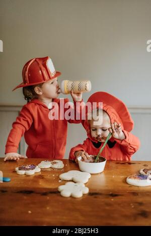 Deux enfants vêtus de pompiers à une table pour décorer des biscuits avec des chocolats et des saupoudrés. Banque D'Images