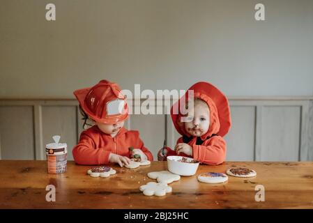 Deux enfants vêtus de pompiers à une table pour décorer des biscuits avec des chocolats et des saupoudrés. Banque D'Images