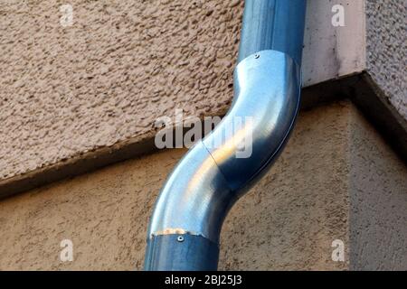 Nouveau tuyau brillant en zink, ligne de rappel d'eau de pluie transfert S coude installé sur le mur extérieur. Système de collecte et de drainage d'eau de pluie. Béton texturé. Banque D'Images