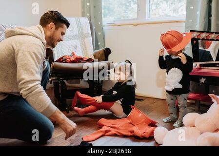 Un père qui aide ses deux enfants à s'habiller comme pompiers. Banque D'Images