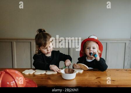 Deux enfants vêtus de pompiers à une table pour décorer des biscuits avec des chocolats et des saupoudrés. Banque D'Images