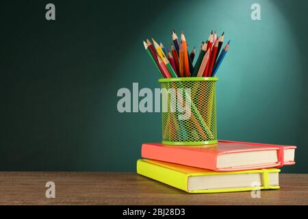 Livres et porte-crayons en métal sur le bureau sur fond de tableau de surveillance vert Banque D'Images