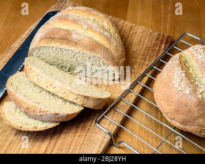 Pain d'avoine fraîchement cuit en tranches, farine de pain blanc et farine d'avoine, surmontée d'avoine roulée sur un plateau à pain en bois Banque D'Images