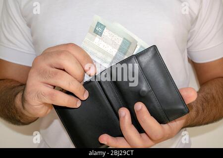 La monnaie nationale de l'Égypte. Billets d'argent. Homme dans un t-shirt blanc a mis des billets de livre égyptien dans le portefeuille noir. Un jeune homme tient dans les mains portefeuille avec e Banque D'Images