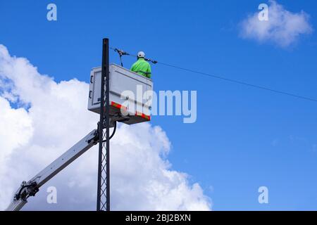 Le Linworker travaille sur des lignes électriques dans le godet de grue dans l'air à partir du levage aérien. Il porte des vêtements fluorescents jaunes pour la sécurité. Journée ensoleillée avec blu Banque D'Images